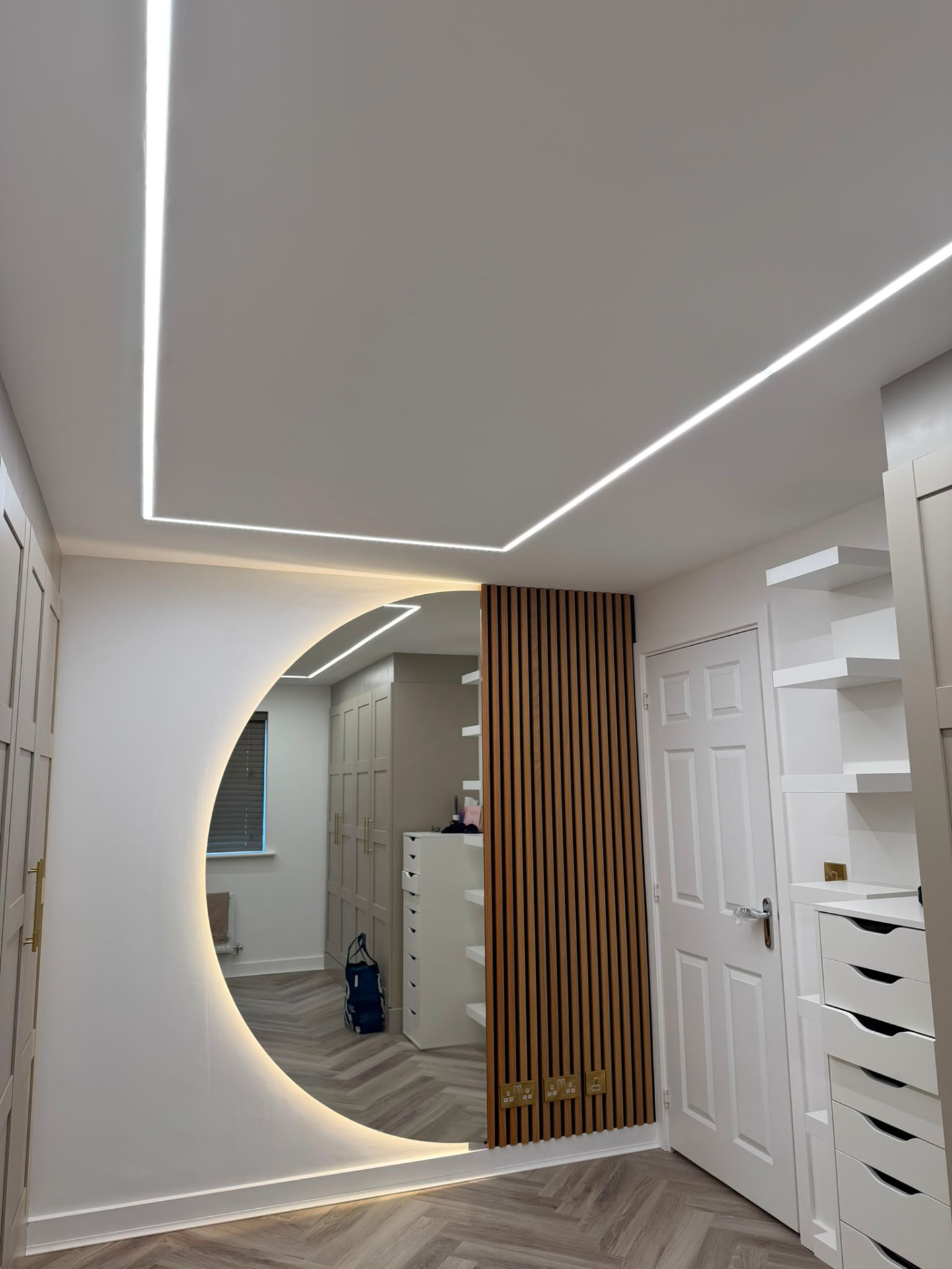 Recessed linear LED lighting and circular backlit mirror in a modern dressing room