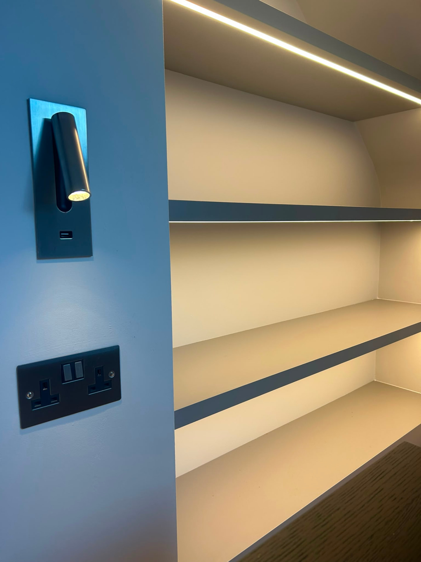 Brushed metal reading light and matt black sockets beside a bed