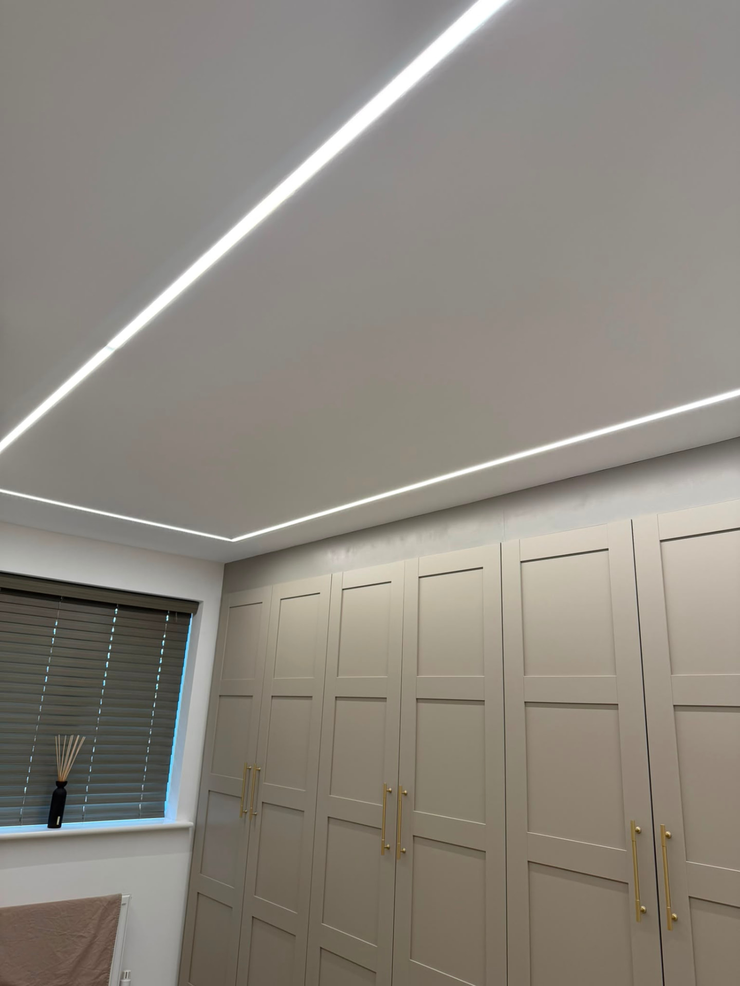 Linear ceiling lighting above fitted wardrobes in a residential bedroom