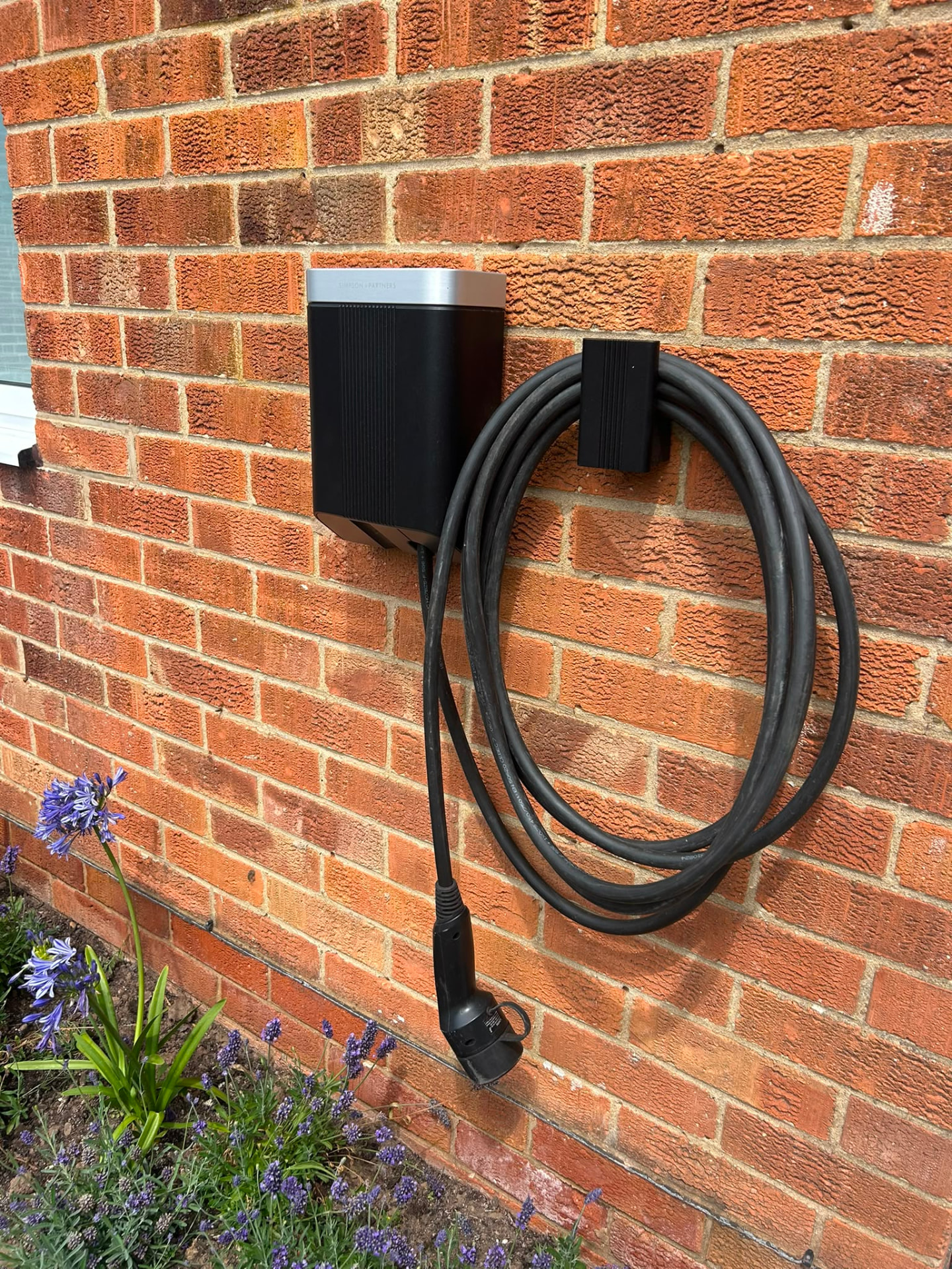 Wall-mounted home EV charger installed on the brick wall of a driveway property
