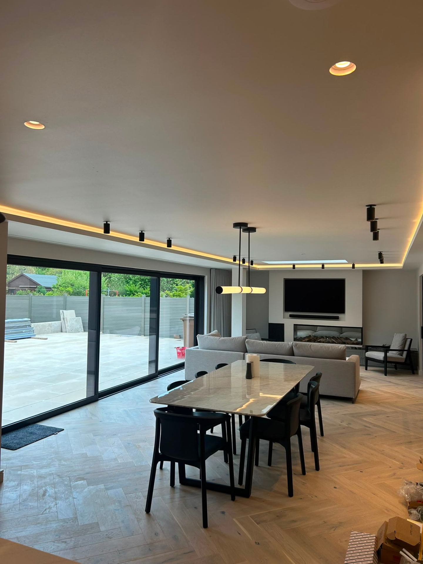 Open-plan living and dining room with warm cove lighting and black track spotlights on a lighting control system