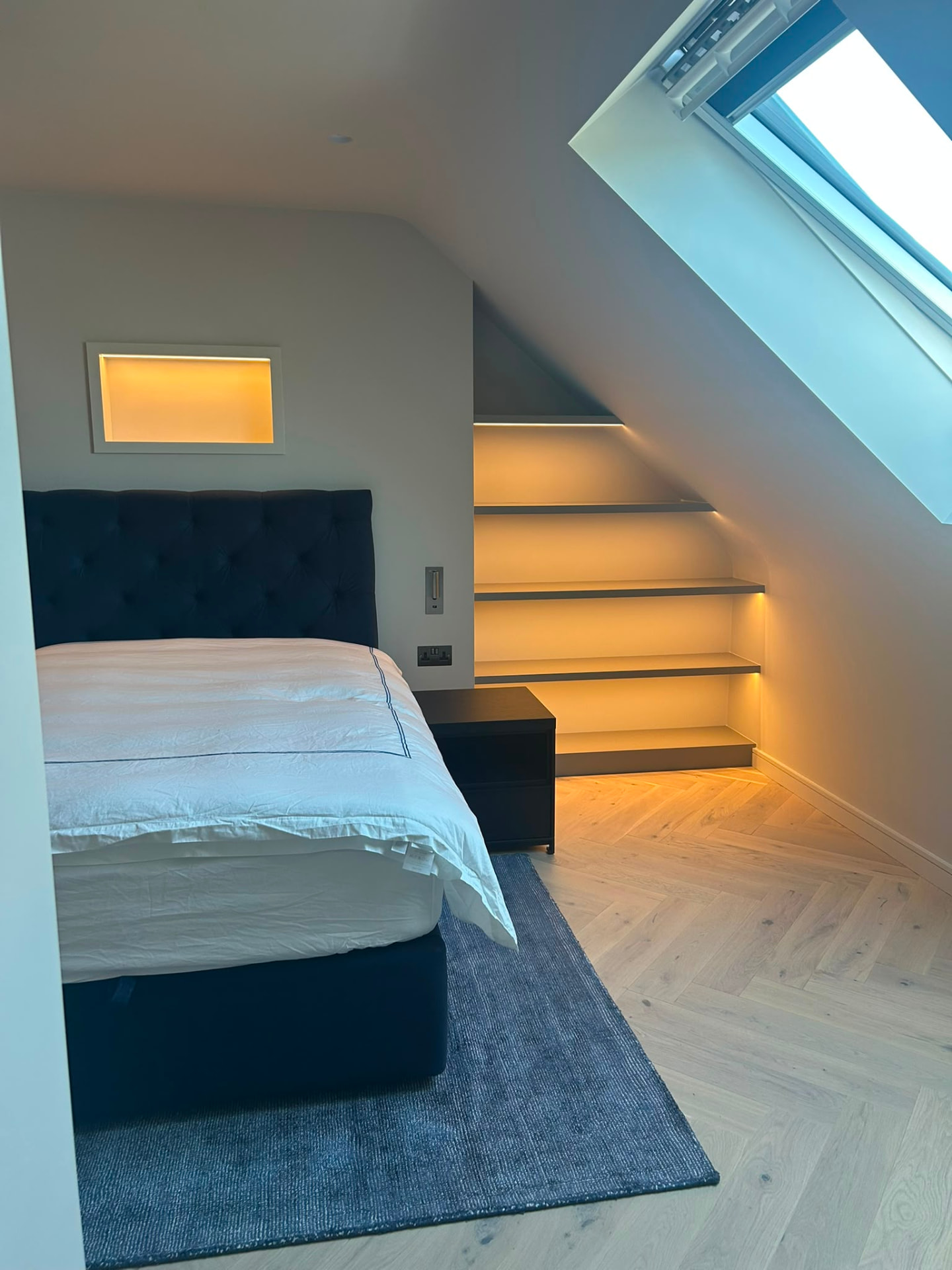 Loft bedroom with warm recessed niche lighting and a backlit headboard panel