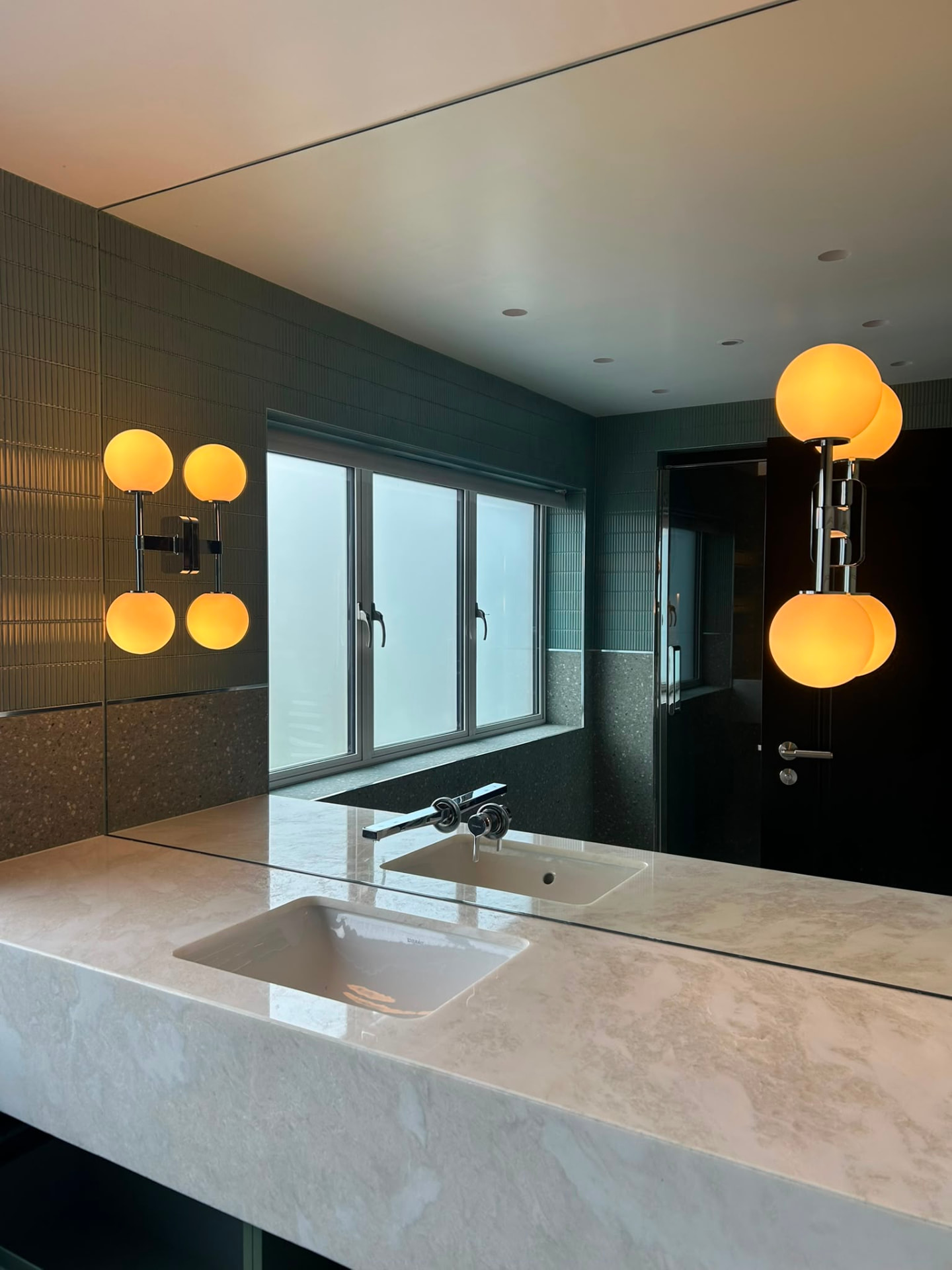 Twin-basin bathroom vanity lit by globe wall sconces either side of large mirrors